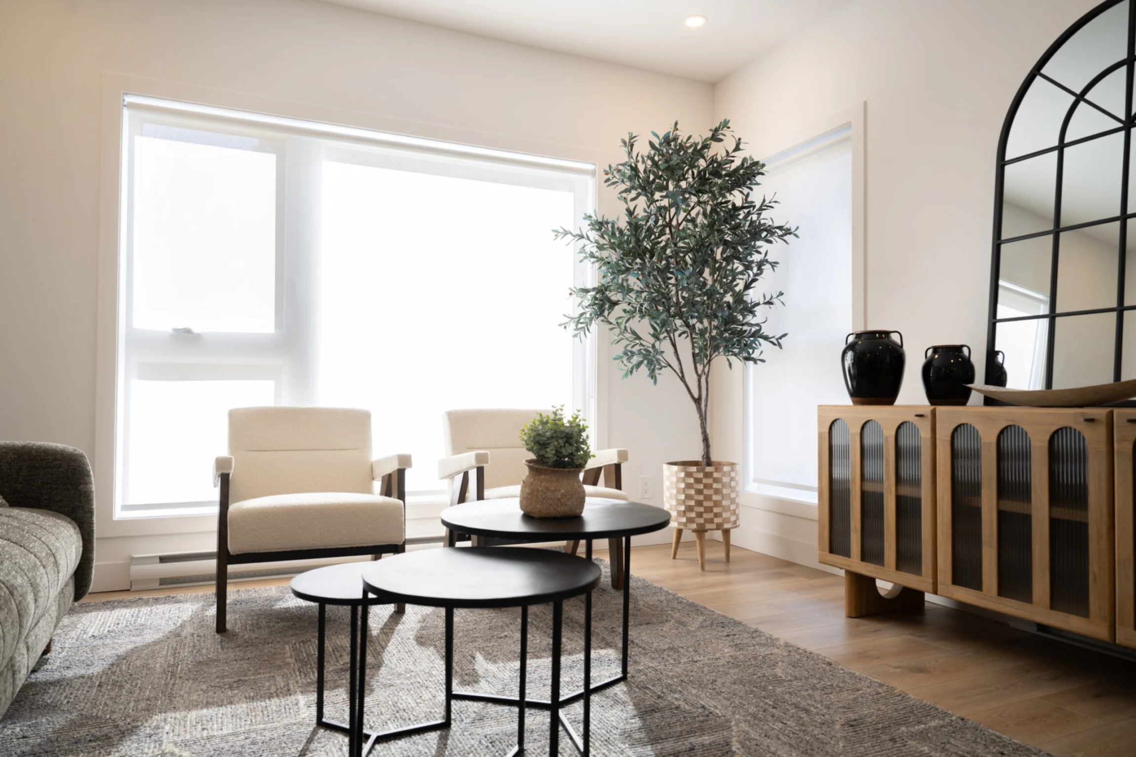 Salon lumineux d'un condo du Quartier Horizon : fauteuils bouclés devant la grande fenestration, miroir arqué et buffet de chêne.